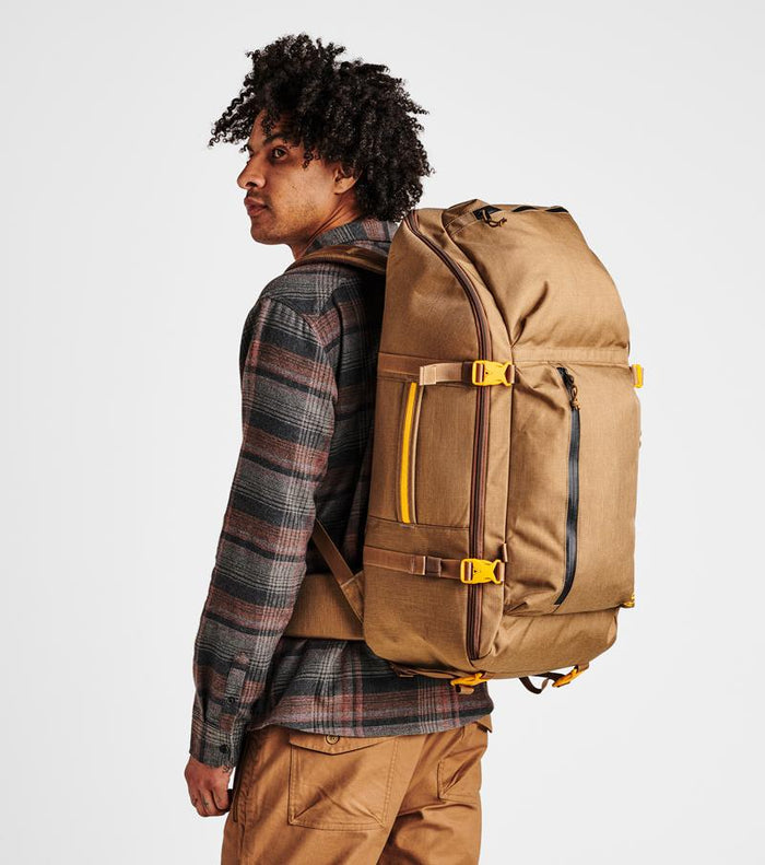 Man holding the Roark 5 Day Mule 55L duffel bag in dark khaki, showcasing its durability.