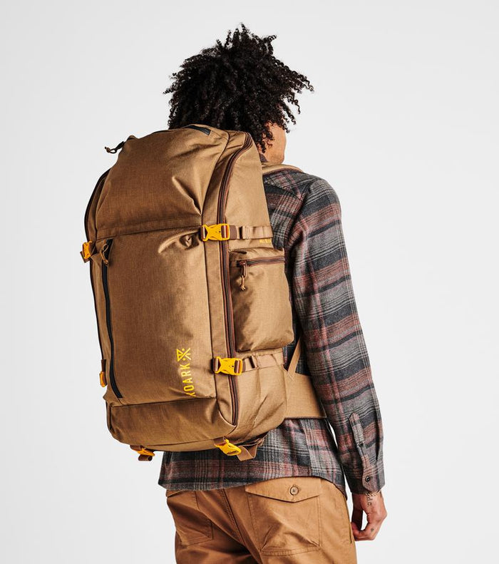 Back view of a man carrying the Roark 5 Day Mule 55L duffel bag in dark khaki, showing off its comfortable fit.