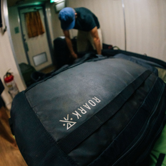 Roark Accomplice Mule 45L backpack in black with logo visible on main compartment, shown in lifestyle setting