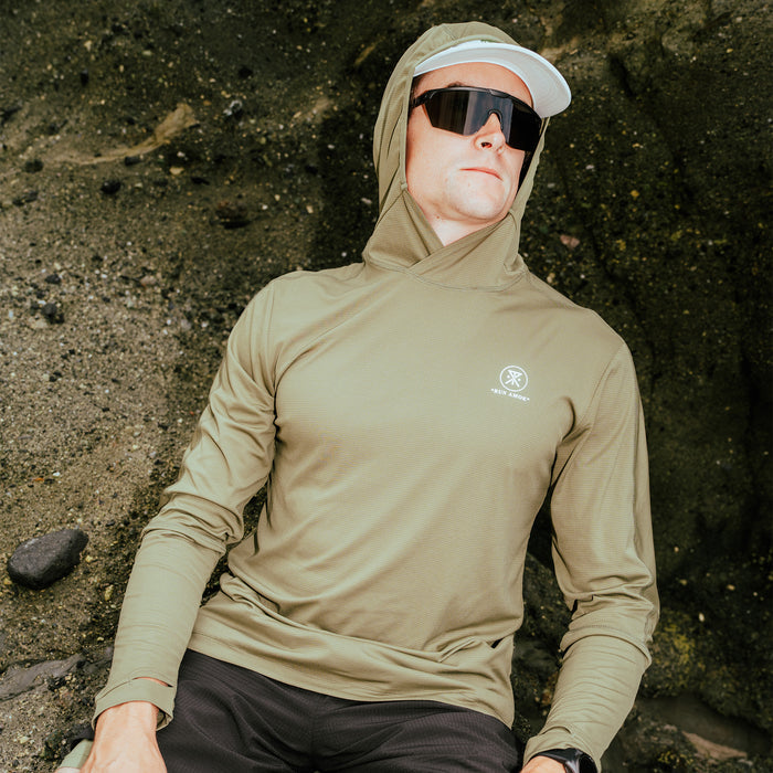 Tan Alta Elite Trail Hood with attached light military colored hood, worn by man against weathered concrete wall with sunglasses and white
