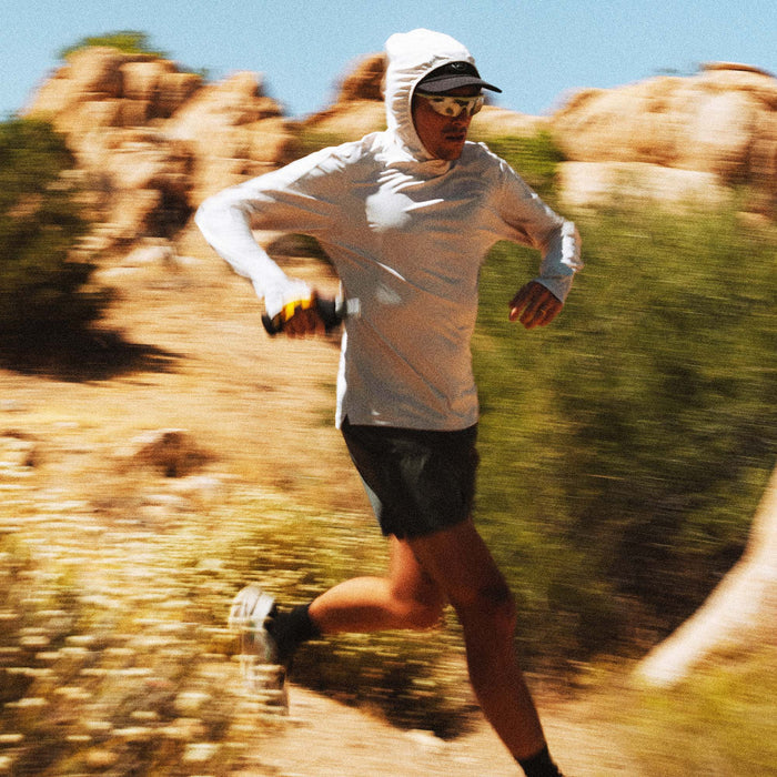 Man wearing Moonstone Alta Elite Trail Hood with white sleeves running on rocky desert trail in motion