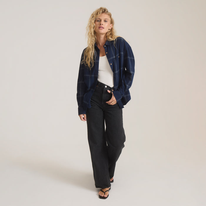 Deep navy plaid flannel shirt with mother-of-pearl buttons worn open over white tank top on model with black jeans