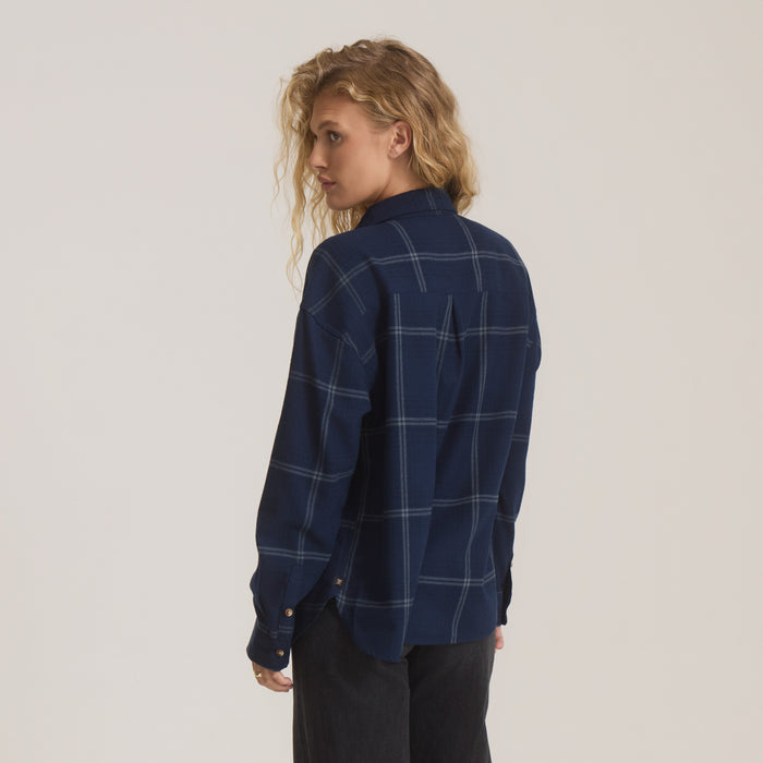 Woman wearing deep navy plaid flannel shirt with light blue windowpane pattern, shown from behind against neutral background