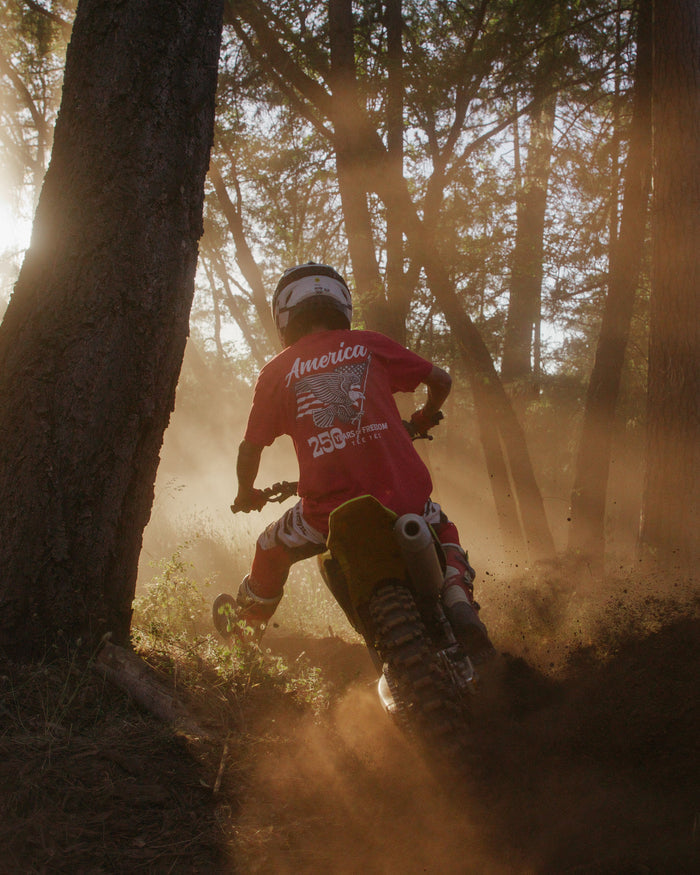 Person riding a dirt bike through a forest with dust in the air