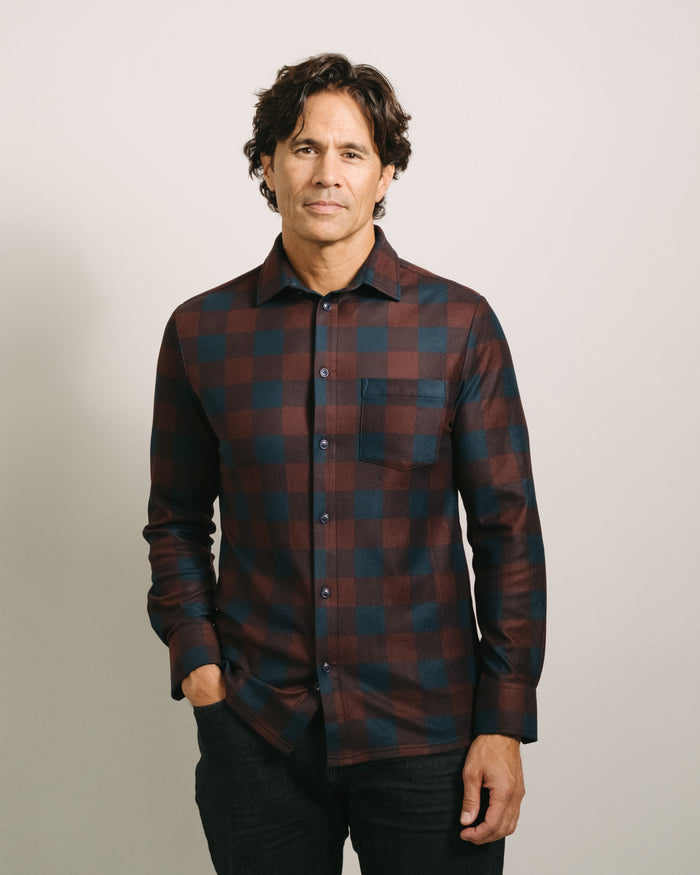Man wearing a mulberry paid (red and black plaid) flannel shirt against a plain background