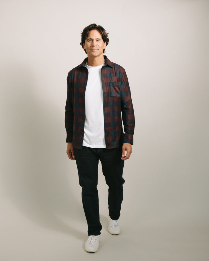 Man wearing a mulberry plaid flannel over a white t-shirt with black pants and white sneakers on a plain background