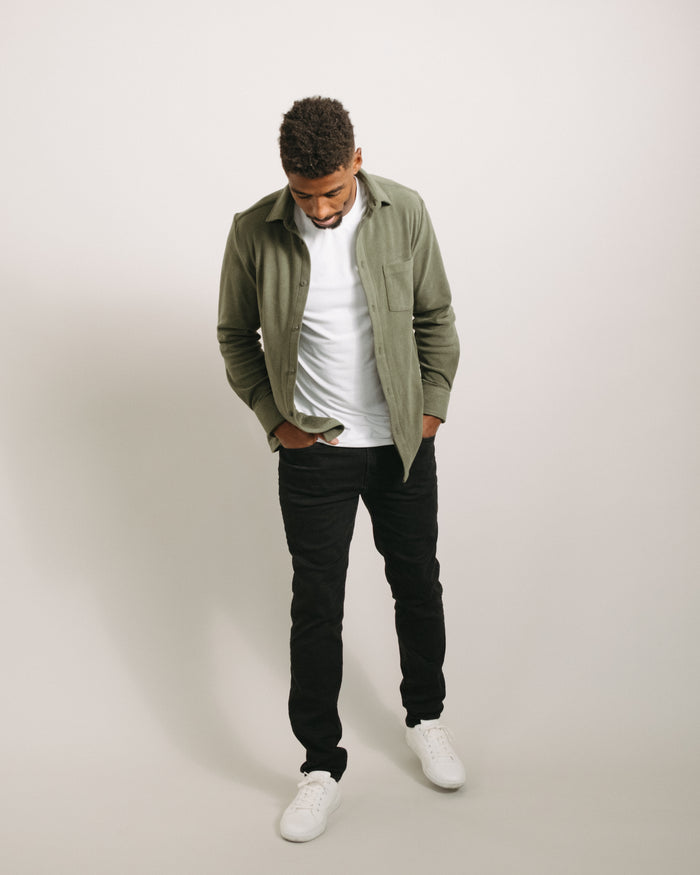 Man wearing a pine green flannel shirt, white t-shirt, black pants, and white sneakers on a plain background