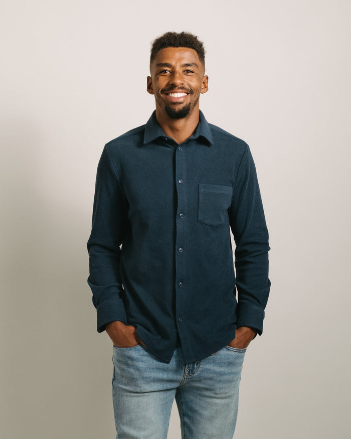Man wearing a storm blue flannel button-up shirt  and light blue jeans against a plain background