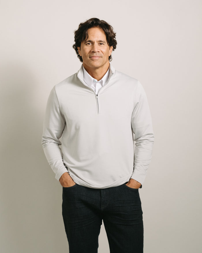 Man wearing a fog light gray quarter-zip sweater over a white shirt with dark pants on a plain background