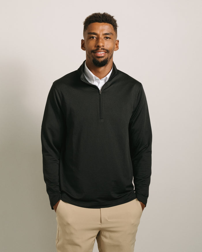 Man wearing a jet black long-sleeve quarter zip and beige pants against a plain background