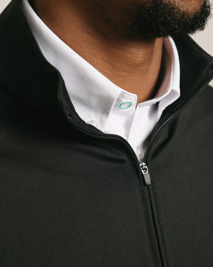 Close-up of a person wearing a jet black long-sleeve quarter zip over a white shirt with a visible brand logo.