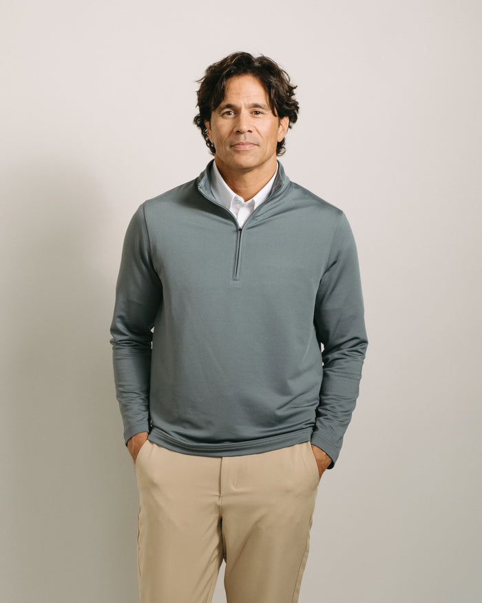 Man wearing a steel gray long-sleeve quarter zip with a white shirt underneath on a plain background
