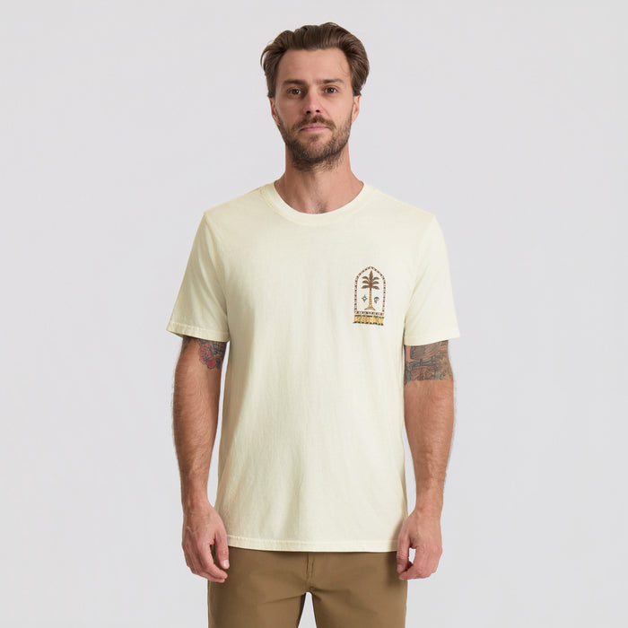 Cream colored short sleeve t-shirt with small decorative palm arch graphic on chest, worn by male model with tattoos
