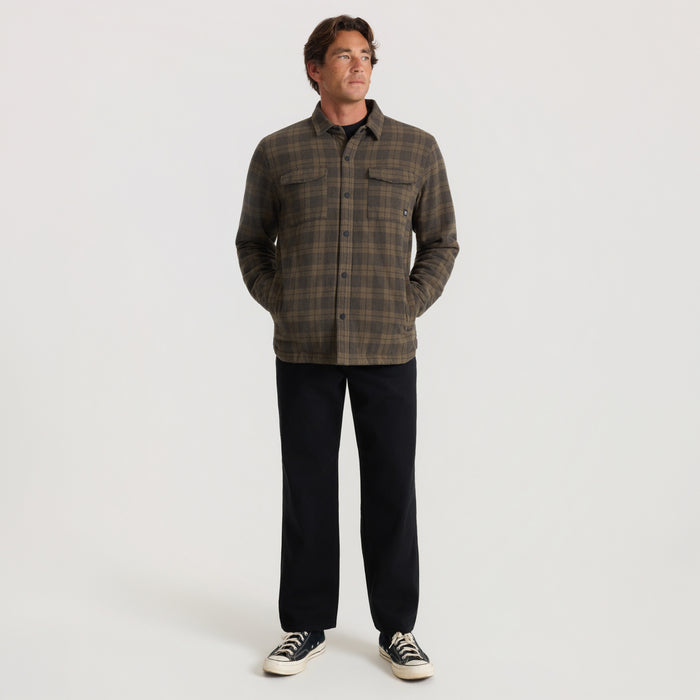 Backwoods Jacket in military plaid worn by man standing against neutral background with black pants and sneakers