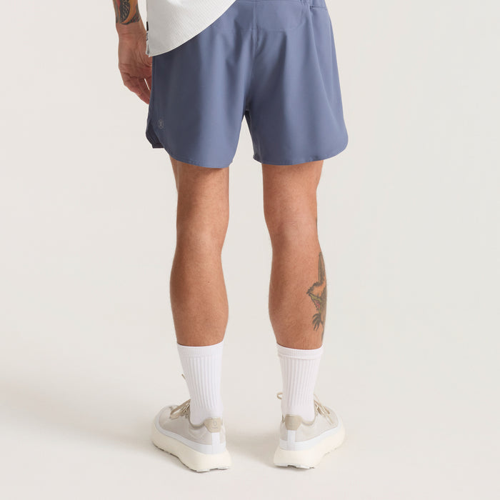 Active man wearing versatile Roark Bermuda shorts, ideal for outdoor adventures and travel, shown in a dynamic running pose.