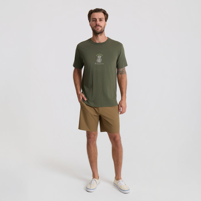 Man standing in a rugged outdoor setting wearing active shorts and a military-style shirt, ready for adventure.