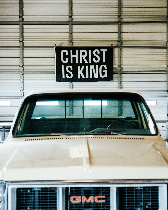 Vintage GMC truck with 'Christ is King' sign above it in a garage.
