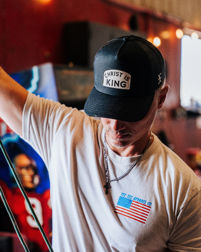 Man wearing a cap and t-shirt with a logo, standing indoors.