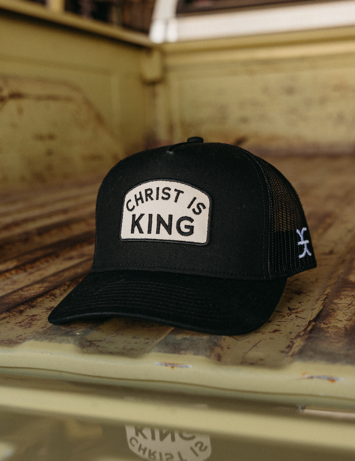 Black cap with 'Christ is King' patch on a rusty surface