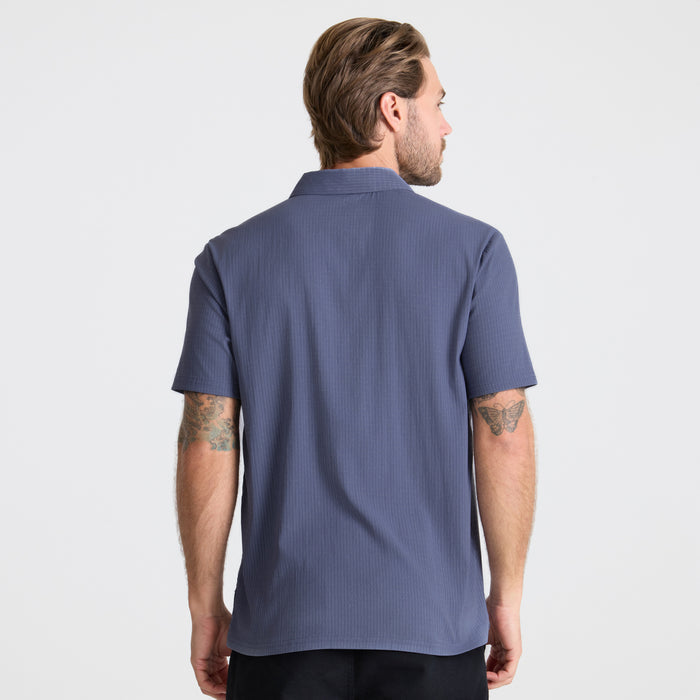 Close-up image of a stylish Roark men's active polo shirt showing details like the sleeve, collar, and buttons, designed for adventure and travel.