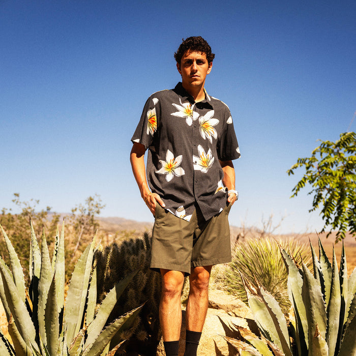Man wearing charcoal short-sleeve shirt with white and yellow floral print, standing in desert landscape with agave plants