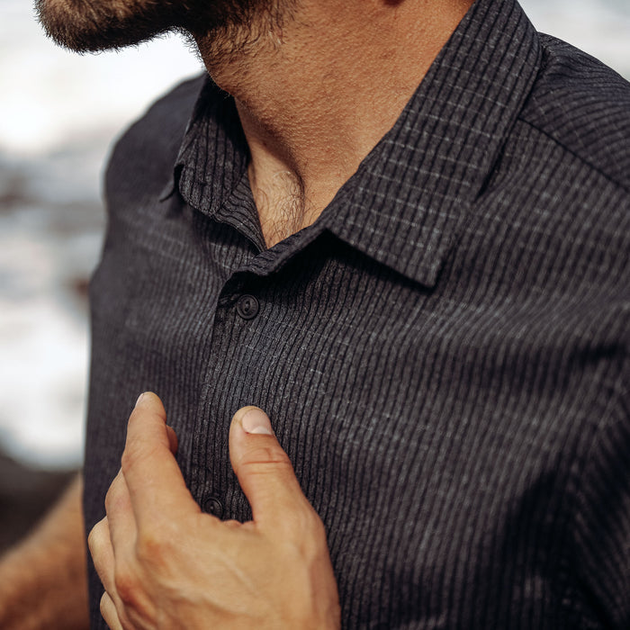 Close-up detail of a black Roark dress shirt focusing on the high-quality textile, sleeve, collar, and buttons, perfect for adventure and travel.
