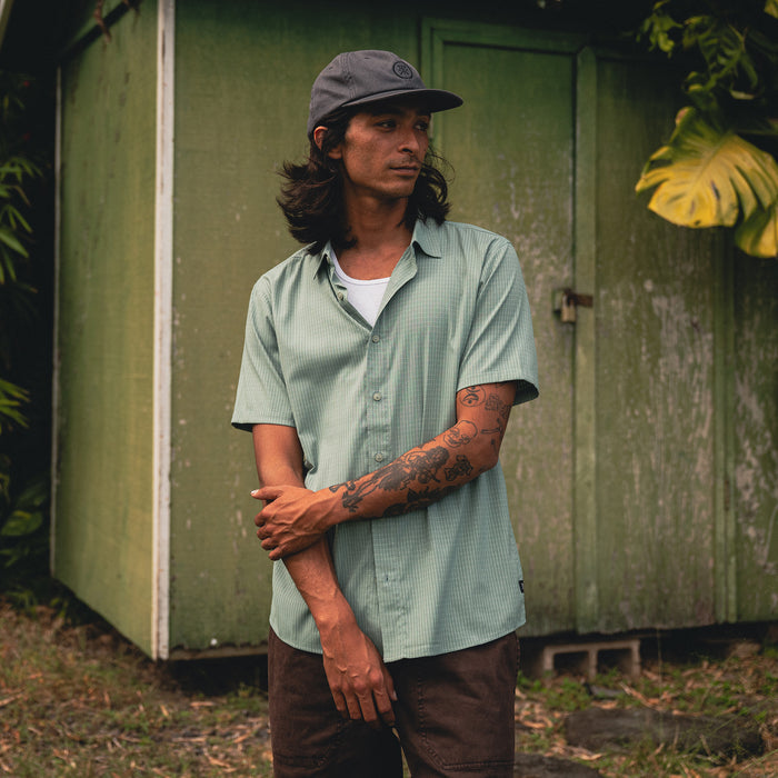 Model showcasing the Bless Up shirt from Roark, featuring detailed collar and sleeve design, styled with outdoor-inspired headgear for adventure travelers.