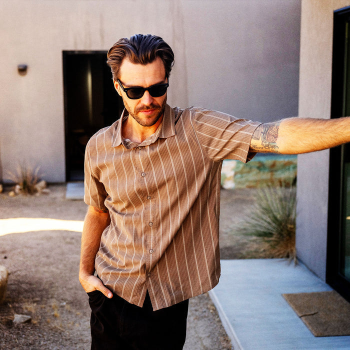 Man wearing mushroom striped short sleeve button-up shirt with black sunglasses in outdoor courtyard setting