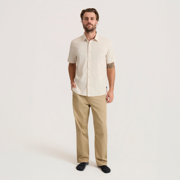 Man wearing sand-colored short sleeve breathable stretch shirt with khaki pants, standing against neutral background