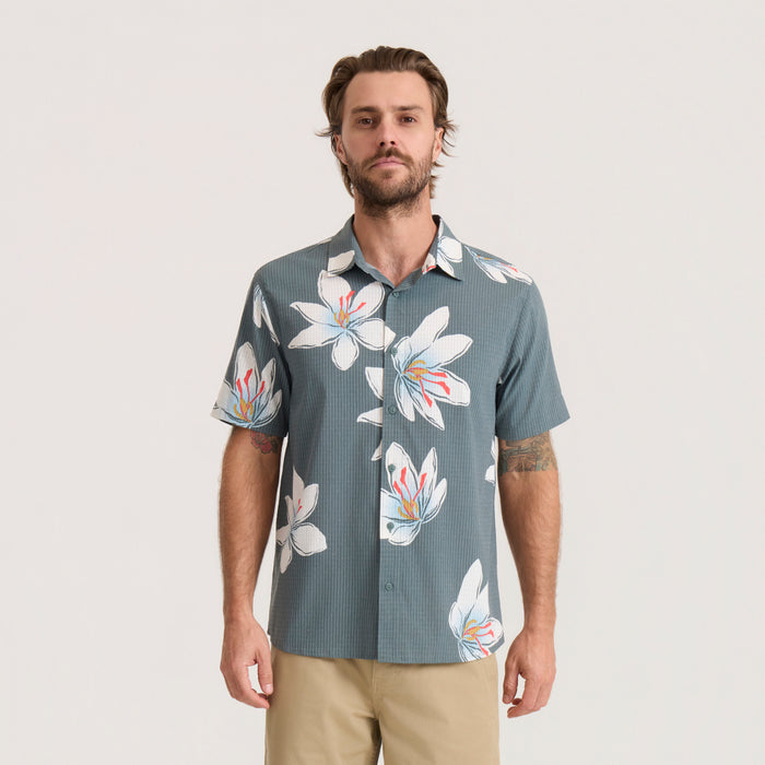 Slate green short-sleeve floral shirt with white and orange flowers worn by man with tan pants, front view