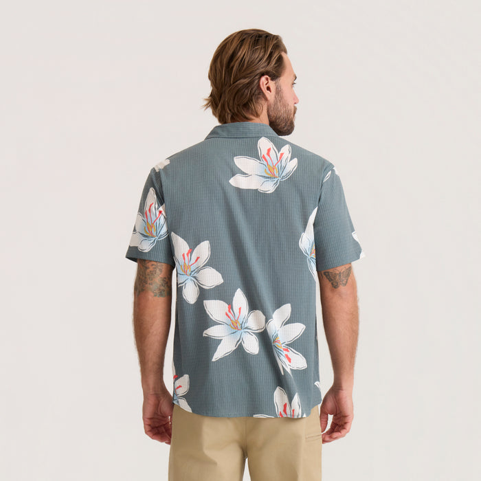 Slate green breathable stretch shirt with white floral print, displayed on male model from back view wearing tan pants