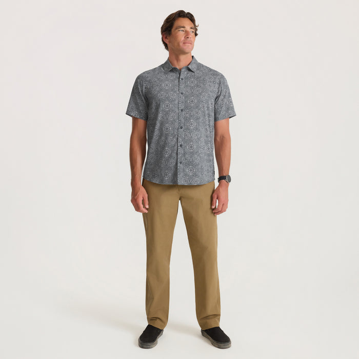 Man wearing slate gray patterned short-sleeve button-up shirt with khaki pants, standing against white background