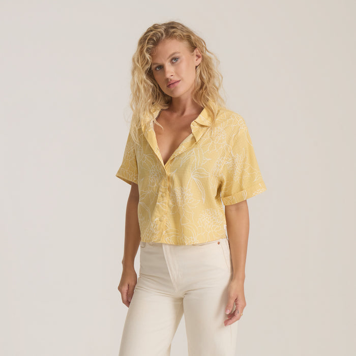 Yellow and white striped camp collar button-up shirt on model with cream pants against neutral background