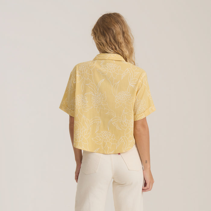 Bless Up Camp Button Up Shirt in wheat yellow with white floral print, worn by model from back view showing short sleeves and cropped fit