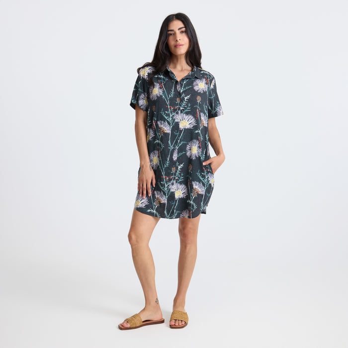 Model in an elegant day dress poses during an outdoor photo shoot, embodying sophistication and adventure.