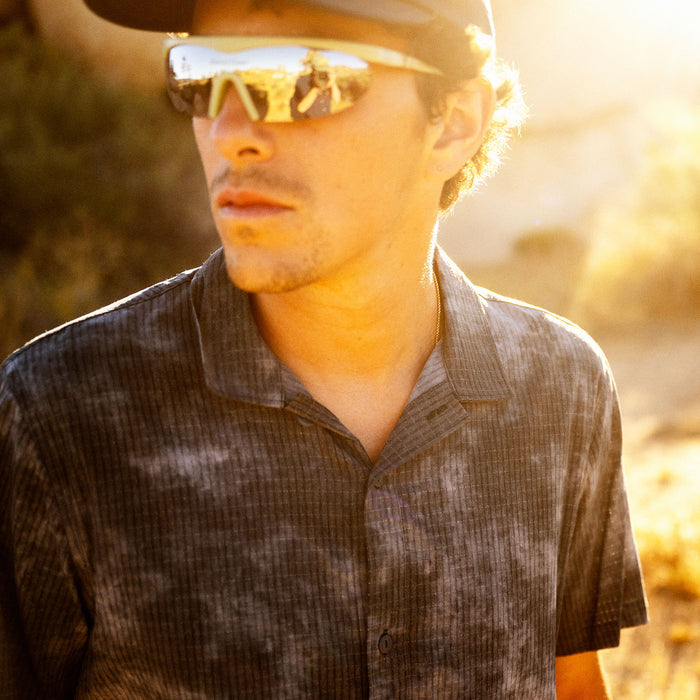 Man wearing dark slate ribbed short-sleeve button-up shirt with yellow-tinted sunglasses outdoors in golden sunlight