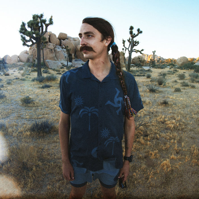 Roark Bless Up Trail button up shirt in ebony blue with palm tree print, worn by man in desert landscape with Joshua trees
