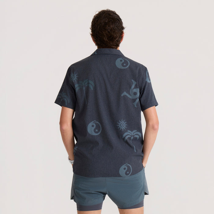 Man wearing back view of Bless Up Trail Button Up Shirt in ebony with blue tonal print and short sleeves