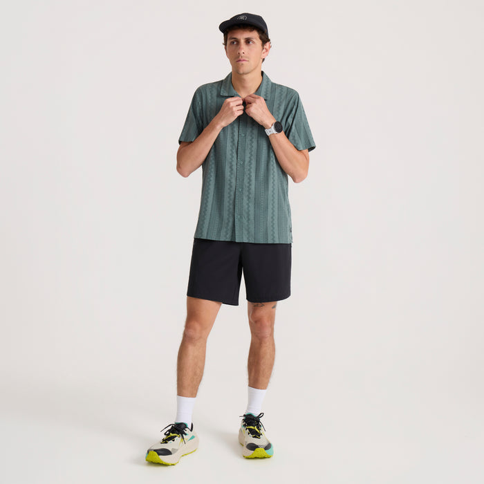 Male model wearing slate green pinstriped short sleeve button-up shirt with black shorts and white socks