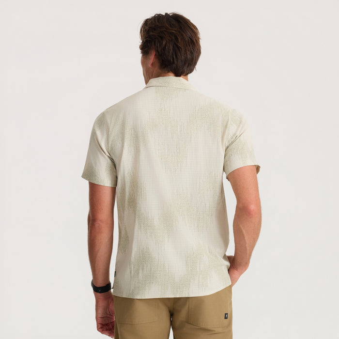 Man wearing Bless Up Trail sand button-up shirt with short sleeves and tan pants, shown from back view