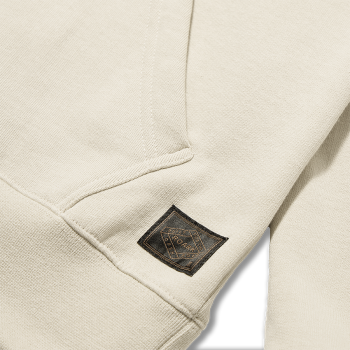 Bolo Fleece Hoodie in Fossil cream with black woven brand label patch on sleeve, detail shot
