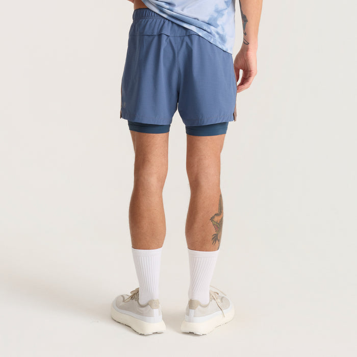 Active person wearing blue Bermuda-style running shorts by Roark, ideal for adventure and travel, showcasing a dynamic mid-action pose.