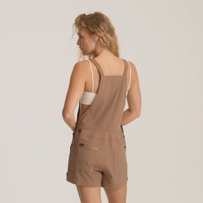 Woman wearing tan Canyon Romper with square neckline, adjustable straps, and cargo pockets, shown from back view