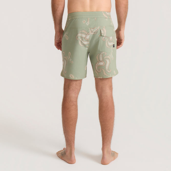 Sage green Chiller Scallop Boardshorts with cream and pink swirl print, shown from behind on male model at beach