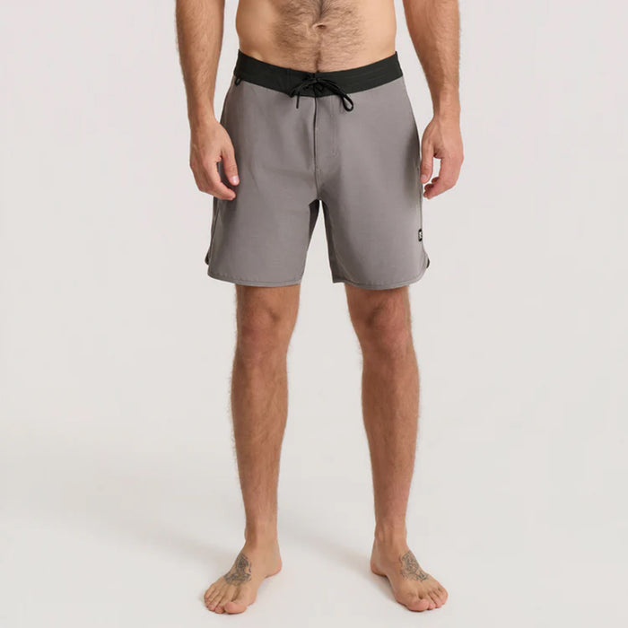 Adventurous man sporting boardshorts, standing by the surf, ready for a seaside adventure, embodying Roark's spirit of travel and outdoor exploration.