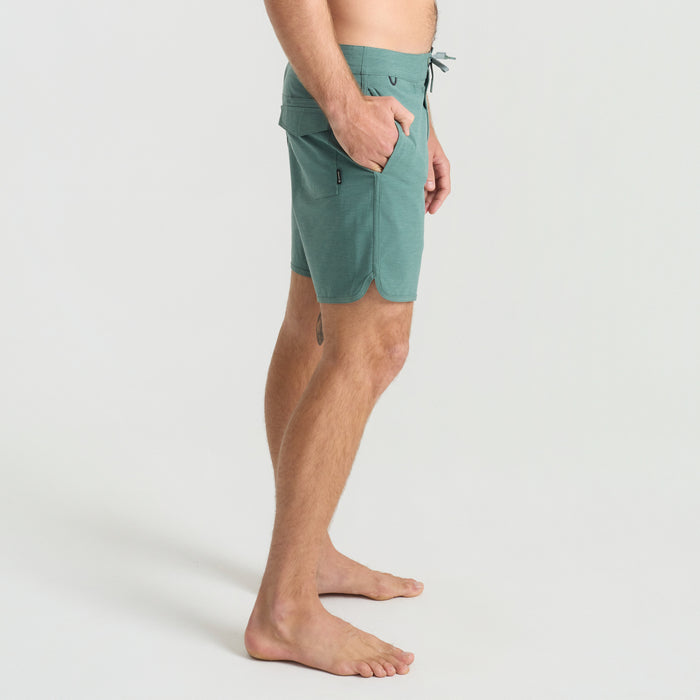 Man walking barefoot on a sandy beach in boardshorts, embodying Roark's adventure and travel spirit.