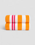 The Classic Stripe Resort Towel Bundle by Cozy Earth, in Picante Stripe, features two neatly folded towels with bold orange, white, and pink stripes stacked together against a plain light gray background.|Color:Picante Stripe