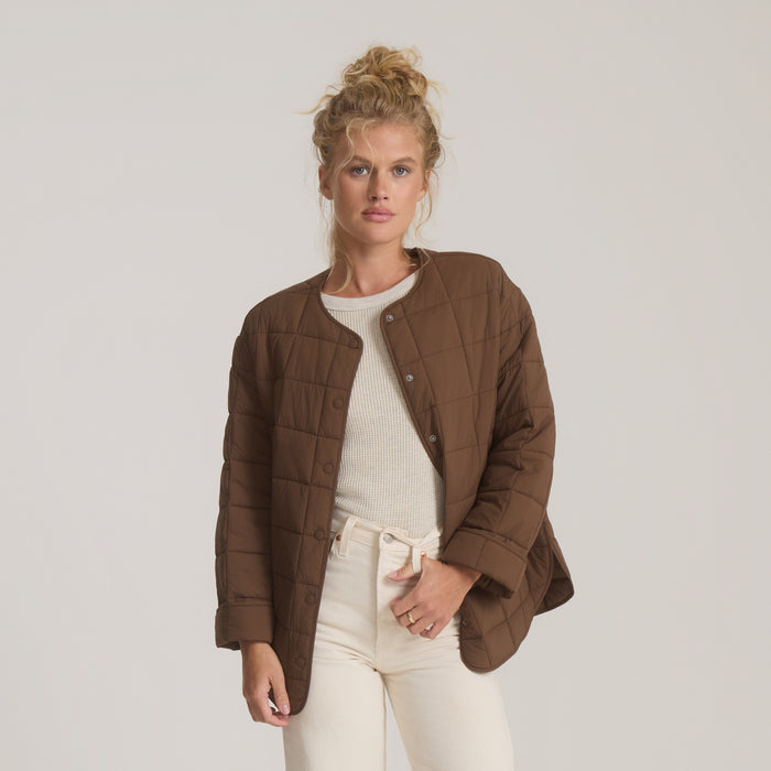 Brown quilted Cloud Liner jacket worn over white ribbed top with cream pants on model against neutral background