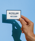 Hand holding a gift card with that says &Collar, Feel Amazing, Gift card against a blue background