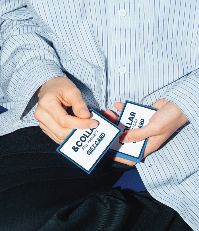 Close up of a person's hands holding two &Collar gift cards